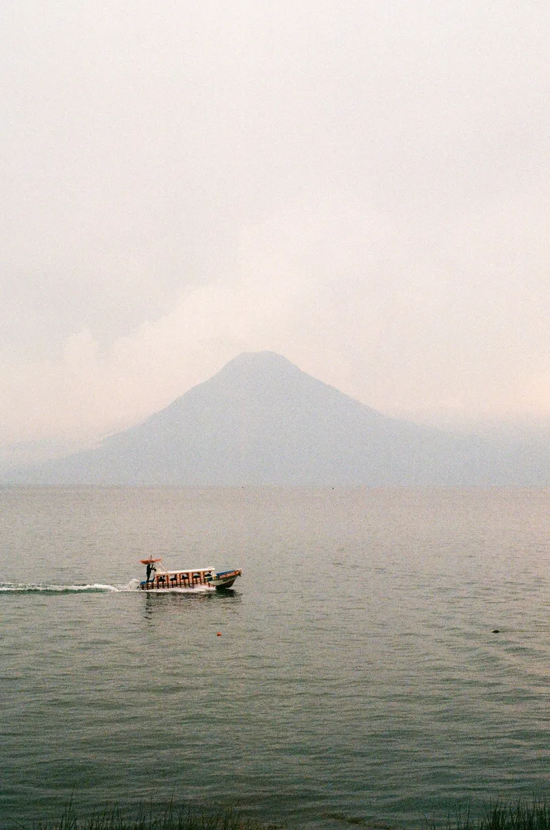 Boat crossing Lake Atitlán below a volcano, Guatemala